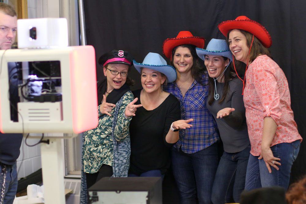 Five people wearing red and blue cowboy hats posing in front of a black backdrop for a photobooth photo