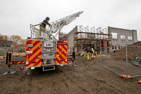 A Plymouth fire truck with ladder extended and a firefighter operating the controls