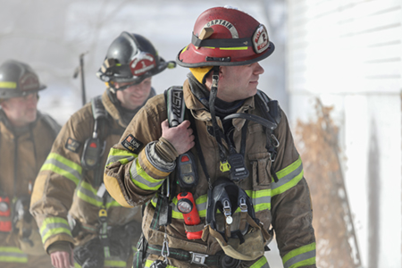 Three Plymouth firefighters walking through a smokey scene