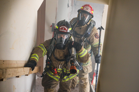 Two firefighters walking up a stairway in a smokey house