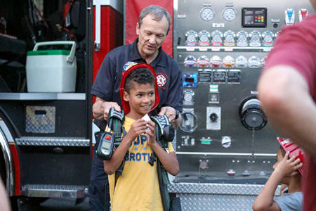 A Plymouth firefighter helping a young resident try on firefighter gear