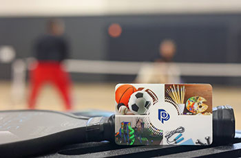 Image of a Parks and Recreation gift card with people playing pickleball blurred out in the background