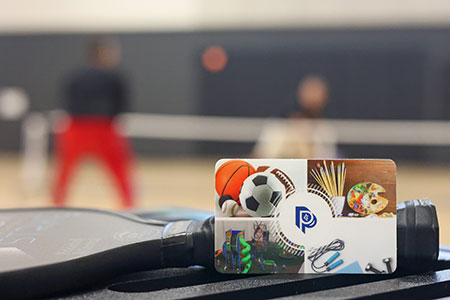 Image of a Parks and Recreation gift card with people playing pickleball blurred out in the background