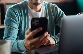 Image of a person holding a smartphone near a computer