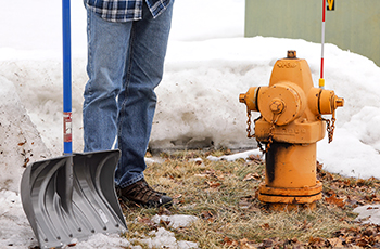 Photo of a person with a shovel standing next to a fire hydrant