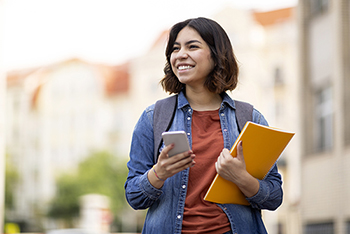 Image of a person holding a smartphone and a notebook wearing a backpack