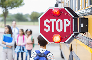 Photo of a school bus stop arm extended, with students in the background