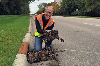 Volunteer cleaning leaves out of a storm drain in Plymouth