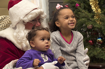 Two children smiling while sitting on Santa Claus' lap during Plymouth's Old Fashioned Christmas event