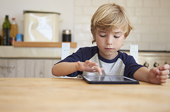 Boy home alone, playing with a mobile tablet device