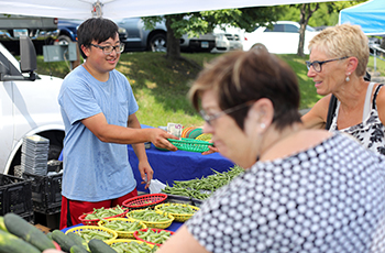 Vendor selling fresh vegetables at the outdoor Plymouth Farmers Market