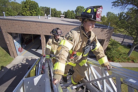 Plymouth firefighters climbing a ladder truck in front of Fire Station 2