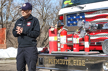 Plymouth Fire Prevention Specialist Steve Marti in front of a fire truck with fire extinguishers